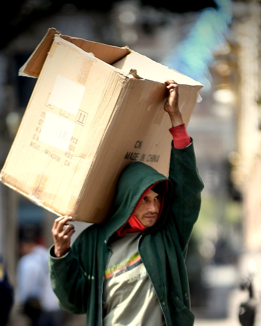 A delivery worker carrying a large cardboard box on one shoulder while unloading a round.