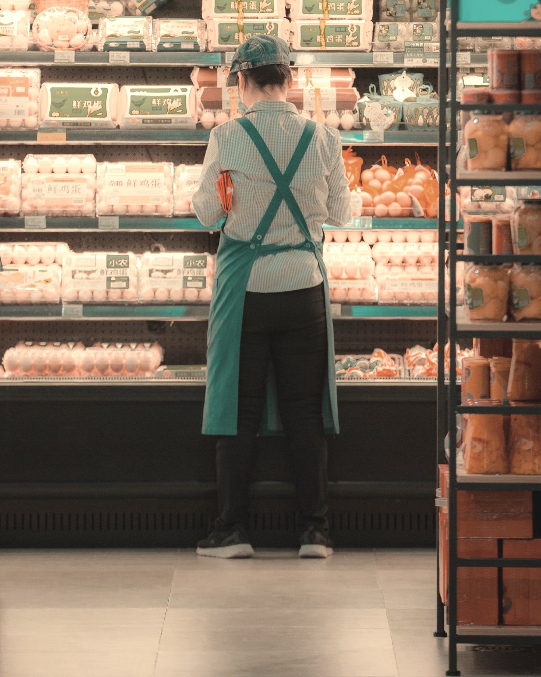 A supermarket worker restocking a chilled shelf during a shift.