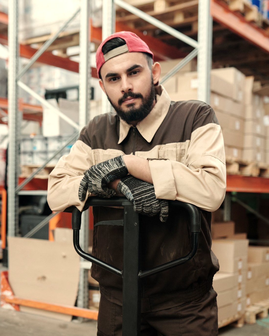 A warehouse worker pausing with both hands resting on a pallet jack handle between lifts.