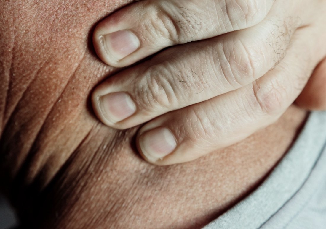 Close, softly lit detail of a person's hand resting against their own shoulder.